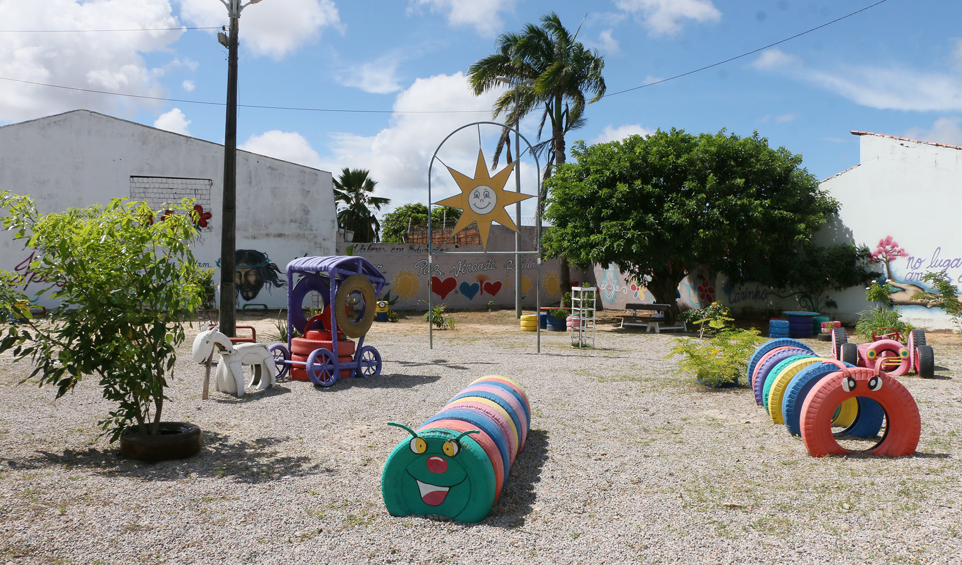 a foto mostra uma visão geral da praça dos ipês com brinquedos feitos de pneus coloridos e plantas